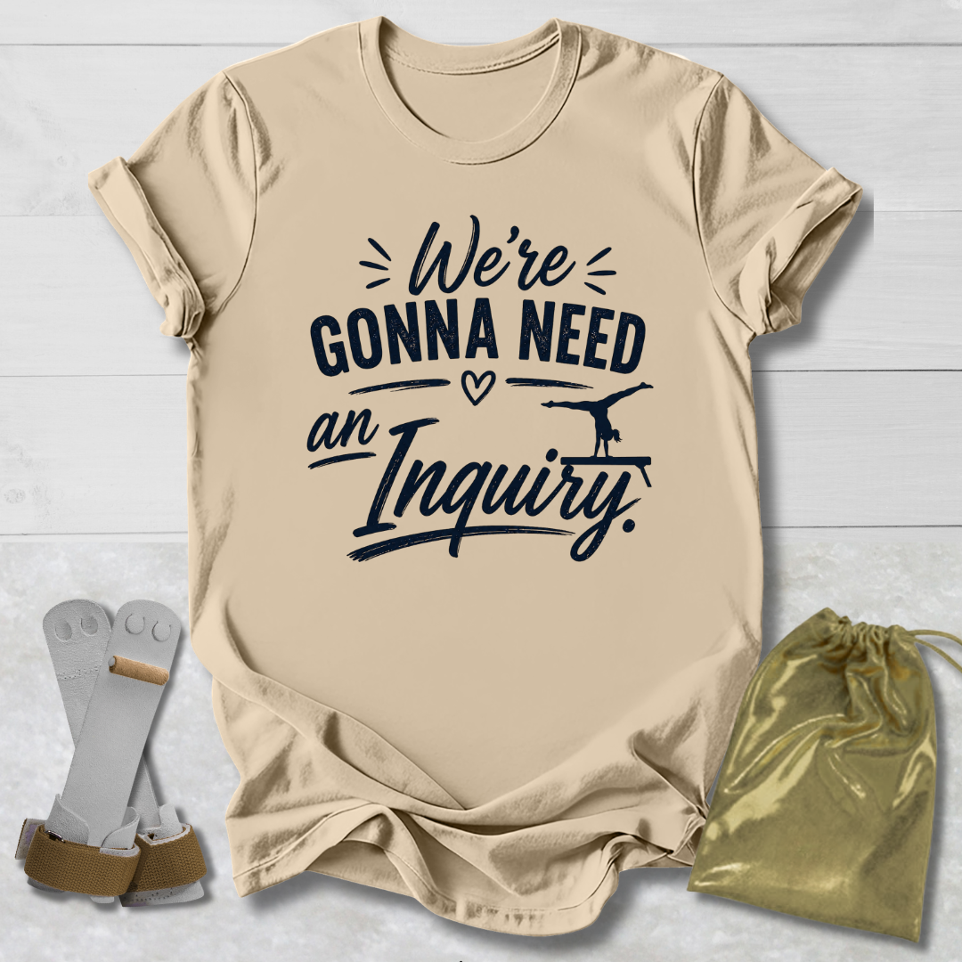 Beige t-shirt with text 'We're Gonna Need an Inquiry' on a light wooden surface with socks and a drawstring bag.