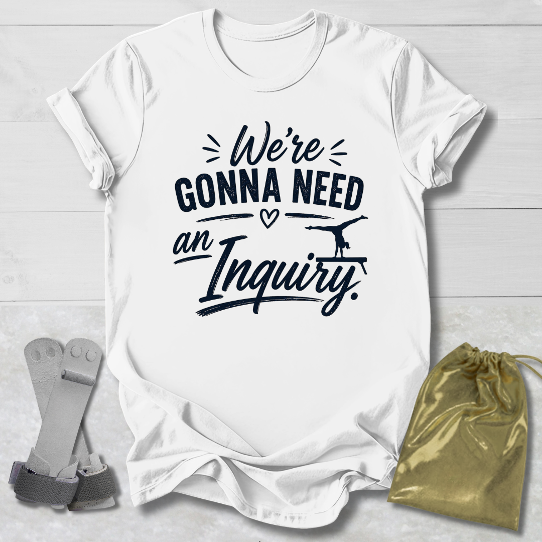 White t-shirt with black text 'We're Gonna Need an Inquiry' on a light wooden surface with socks and a drawstring bag.