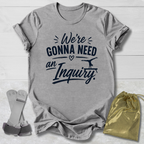 Gray t-shirt with humorous text design on a light wooden surface, accompanied by socks and a drawstring bag.