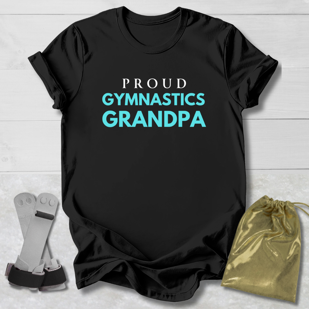 Black t-shirt with 'Proud Gymnastics Grandpa' text on a light wooden surface with socks and a drawstring bag.