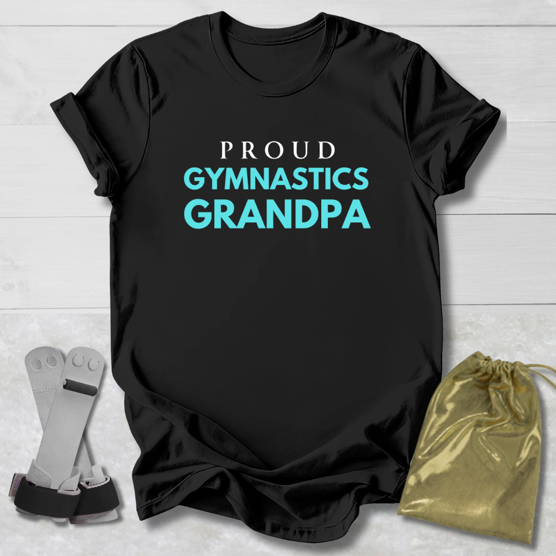 Black t-shirt with 'Proud Gymnastics Grandpa' text on a light wooden surface with socks and a drawstring bag.