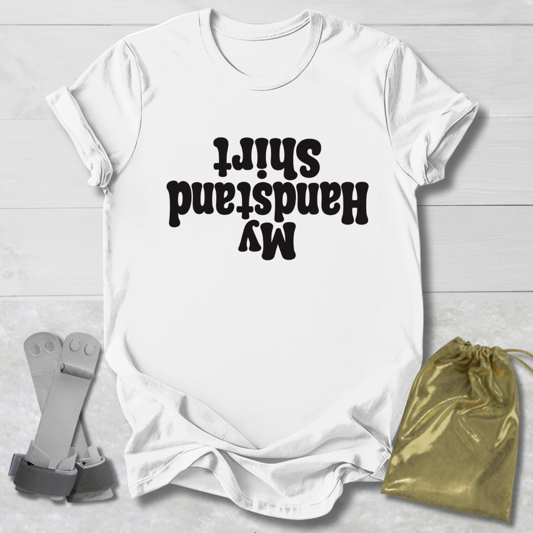 White t-shirt with black My Handstand Shirt text on a light wooden surface with socks and a drawstring bag.