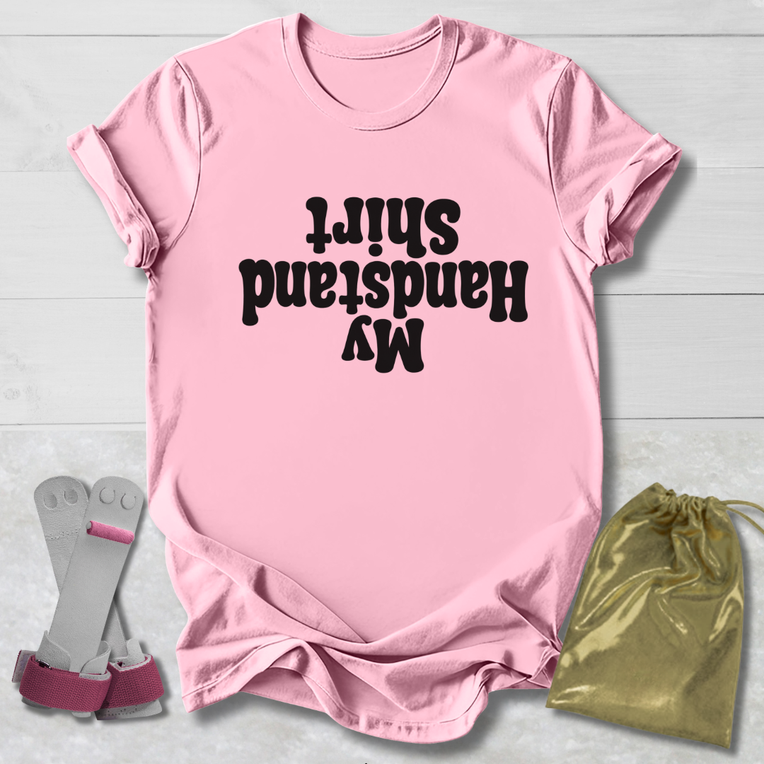 Pink t-shirt with black  My Handstand Shirt text, socks, and drawstring bag on a light wooden surface