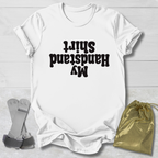 White t-shirt with black My Handstand Shirt text on a light wooden surface with socks and a drawstring bag.