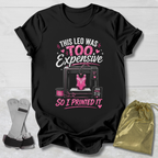 Black t-shirt with pink and white graphic and text on a light wooden surface.