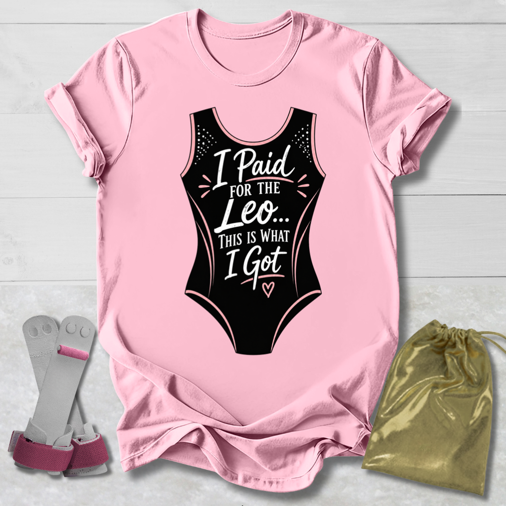 Pink t-shirt with black funny gymnastics leotard graphic and text, socks, and drawstring bag on a light wooden surface.