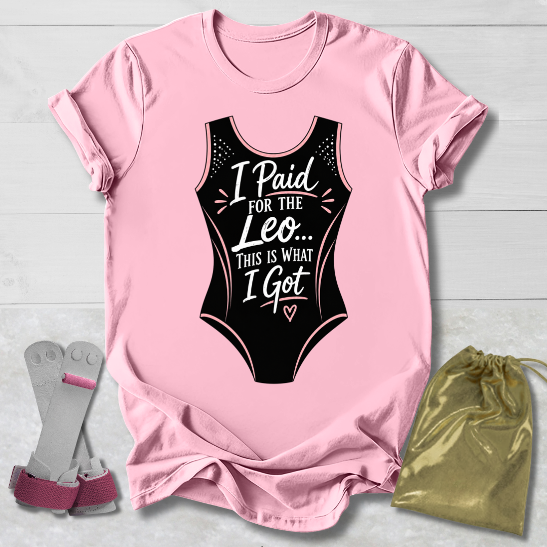 Pink t-shirt with black funny gymnastics leotard graphic and text, socks, and drawstring bag on a light wooden surface.