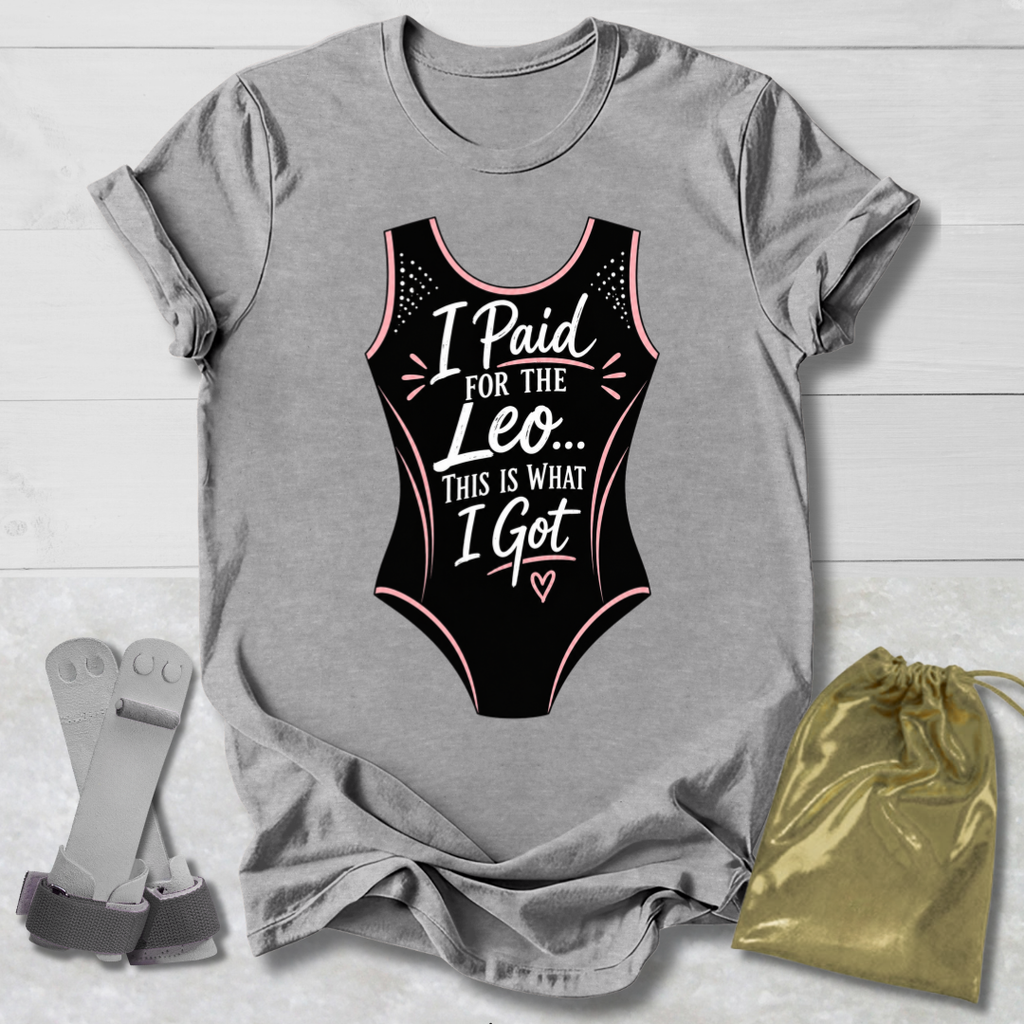 Gray t-shirt with a graphic of a funny gymnastics leotard and text, placed on a light wooden surface with socks and a drawstring bag.