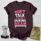 Maroon t-shirt with 'Don't talk to me during beam' text on a light wooden surface.