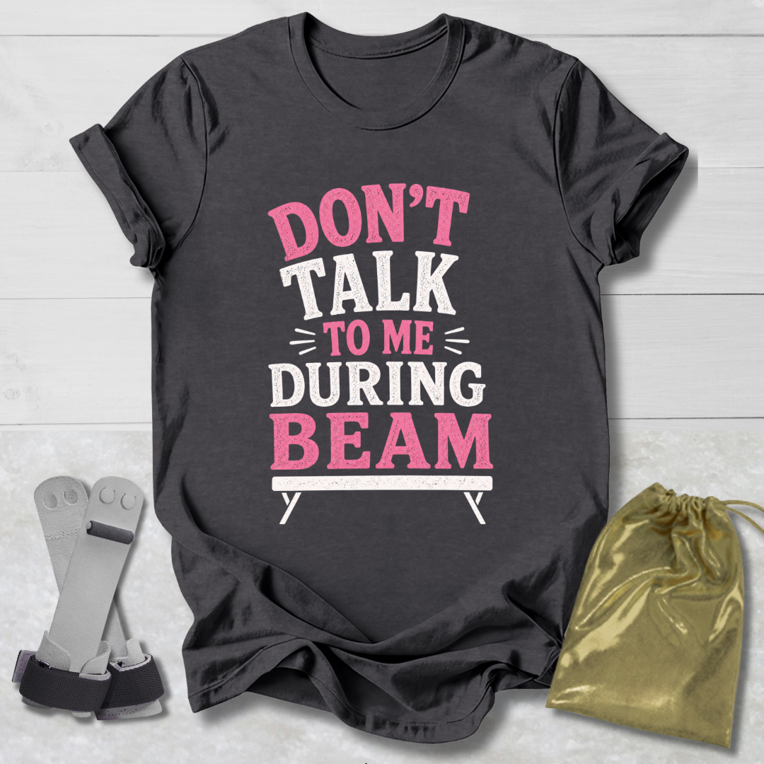 Black t-shirt with pink and white text 'Don't talk to me during beam' on a light wooden surface.