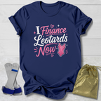 Navy blue t-shirt with pink and white  I finance leotards now gymnastics text and graphics, placed on a light wooden surface with socks and a drawstring bag.
