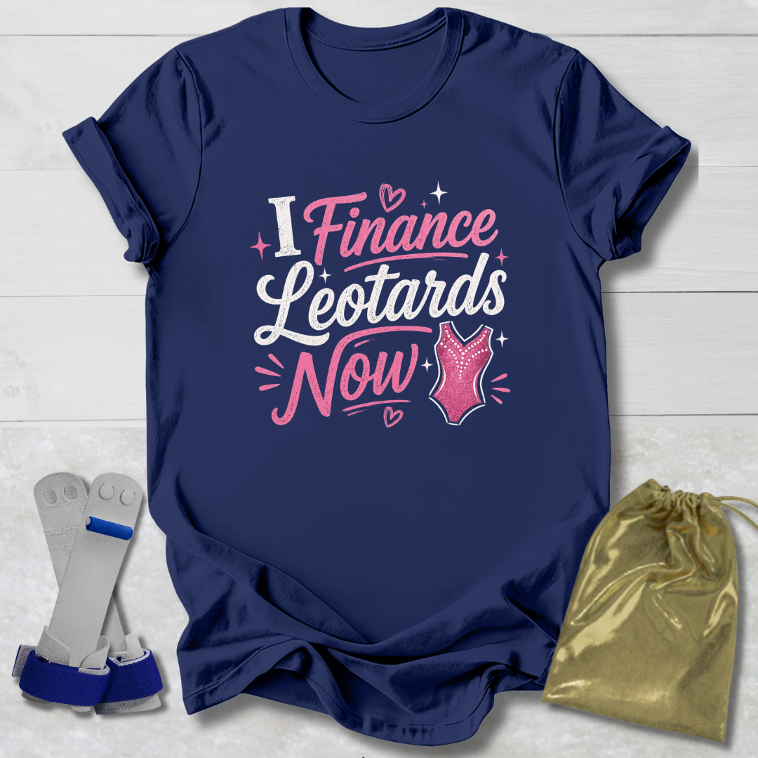 Navy blue t-shirt with pink and white  I finance leotards now gymnastics text and graphics, placed on a light wooden surface with socks and a drawstring bag.