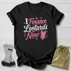 Black t-shirt with pink and white text on a light wooden surface, accompanied by socks and a gold drawstring bag.