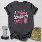 Maroon t-shirt with pink  I finance leotards now gymnastics text and graphics on a light wooden surface, accompanied by socks and a drawstring bag.
