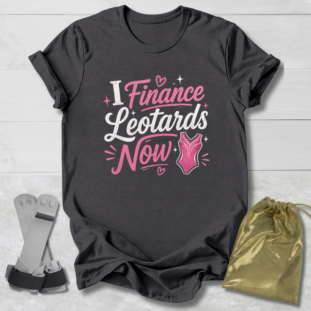 Maroon t-shirt with pink  I finance leotards now gymnastics text and graphics on a light wooden surface, accompanied by socks and a drawstring bag.
