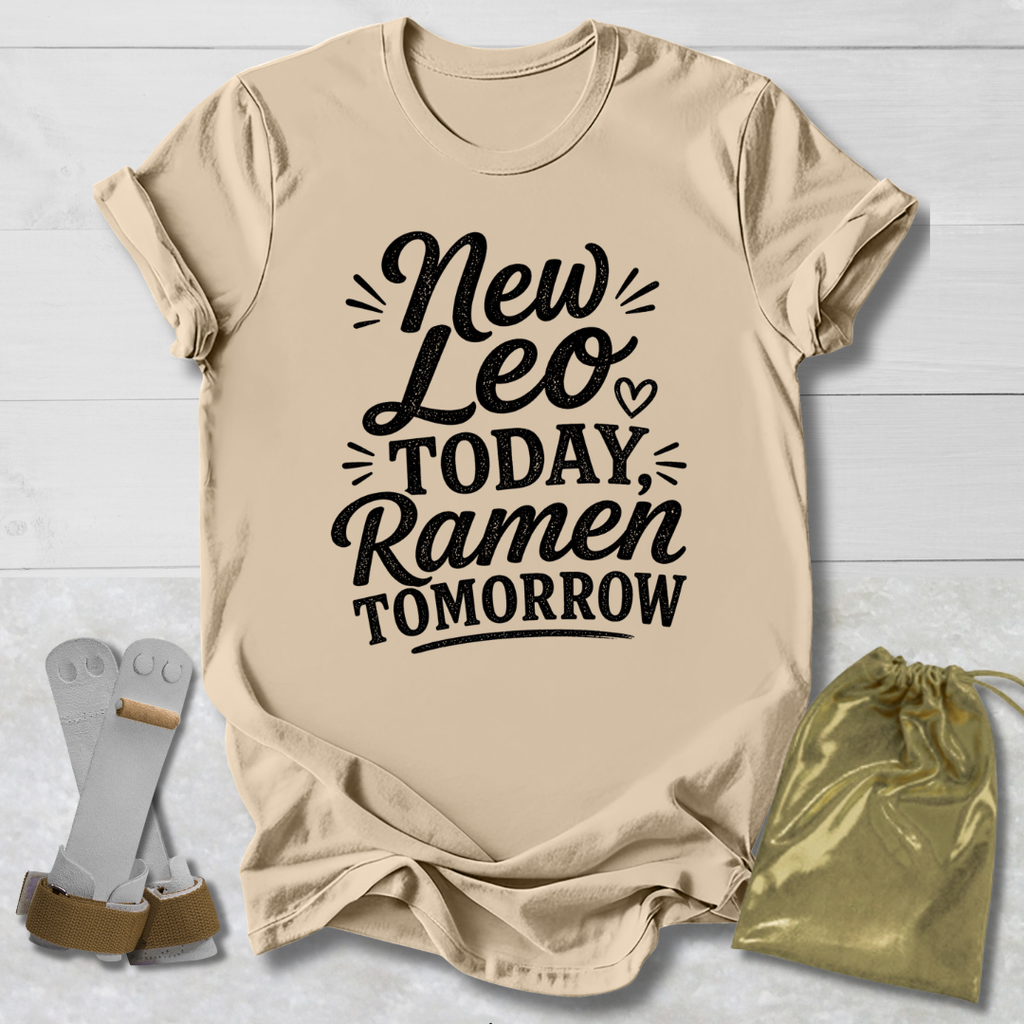 Beige t-shirt with 'New Leo Today, Ramen Tomorrow' text on a light wooden surface with socks and a drawstring bag.