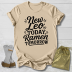 Beige t-shirt with 'New Leo Today, Ramen Tomorrow' text on a light wooden surface with socks and a drawstring bag.