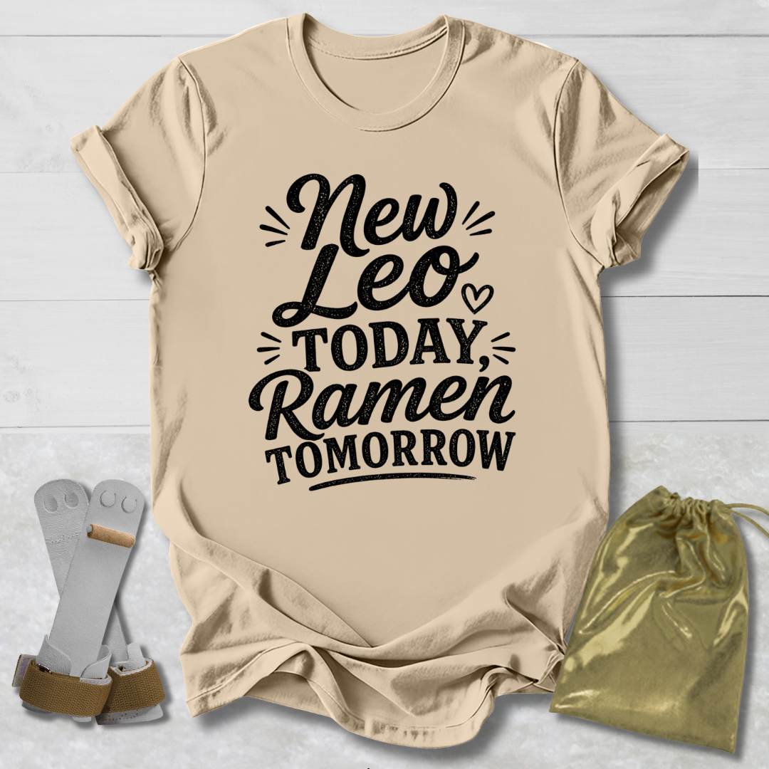 Beige t-shirt with 'New Leo Today, Ramen Tomorrow' text on a light wooden surface with socks and a drawstring bag.