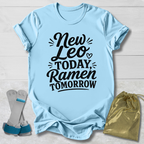 Light blue t-shirt with 'New Leo Today, Ramen Tomorrow' text on a wooden surface with socks and a drawstring bag.