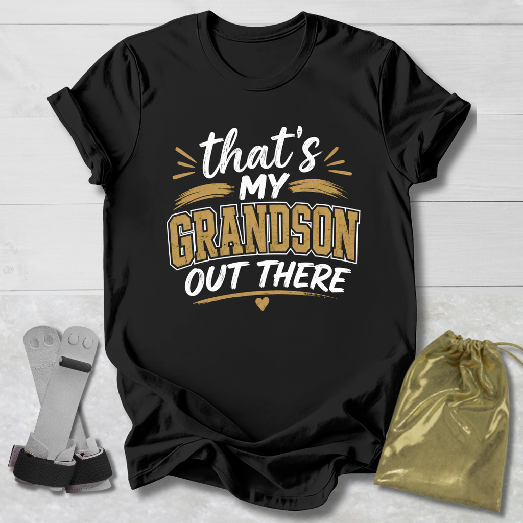 Black t-shirt with 'That's my grandson out there' text on a light wooden surface with socks and a drawstring bag.