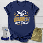 Navy blue t-shirt with 'that's my grandson out there' text, socks, and drawstring bag on a light wooden surface.