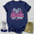 Navy blue t-shirt with 'that's my granddaughter out there' text, socks, and drawstring bag on a light wooden surface.