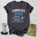 Dark gray t-shirt with 'Gymnastics Dad' text, socks, and drawstring bag on a light wooden surface