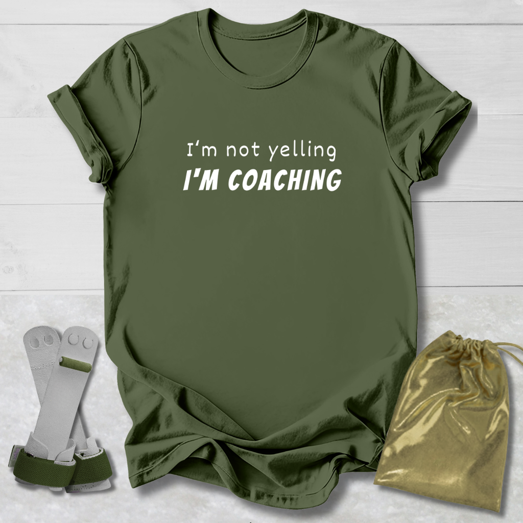 Green t-shirt with 'I'm not yelling I'm coaching' text, socks, and drawstring bag on a light wooden surface.