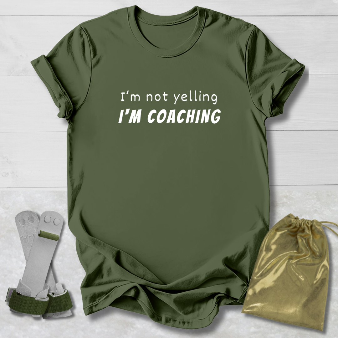Green t-shirt with 'I'm not yelling I'm coaching' text, socks, and drawstring bag on a light wooden surface.