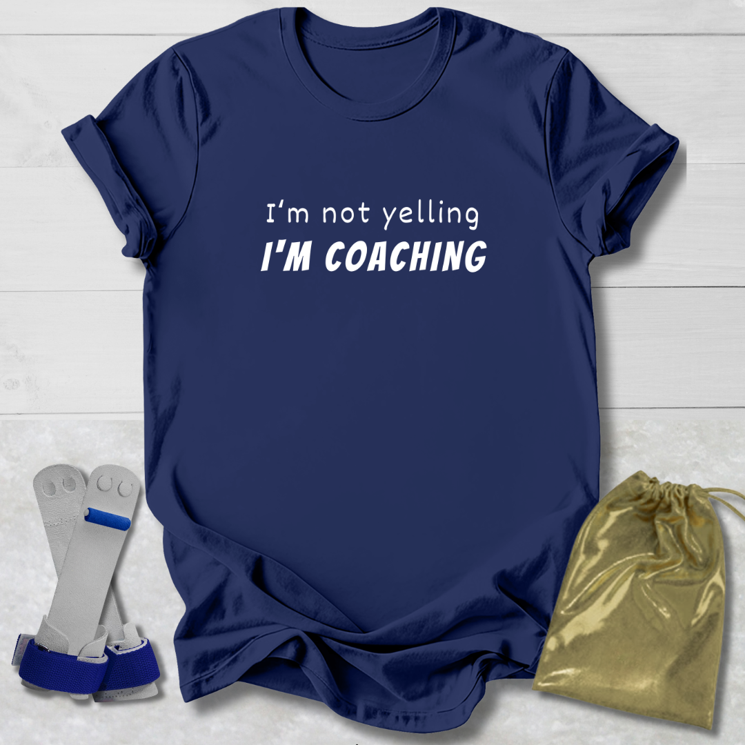 Navy blue t-shirt with 'I'm not yelling I'm coaching' text, socks, and drawstring bag on a light wooden surface.