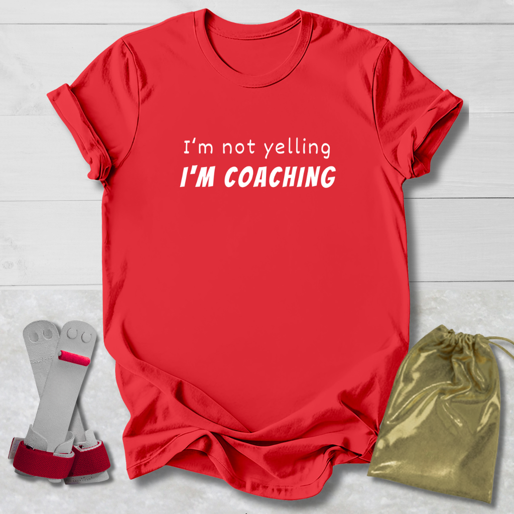 Red t-shirt with 'I'm not yelling I'm coaching' text, socks, and drawstring bag on a light wooden surface.