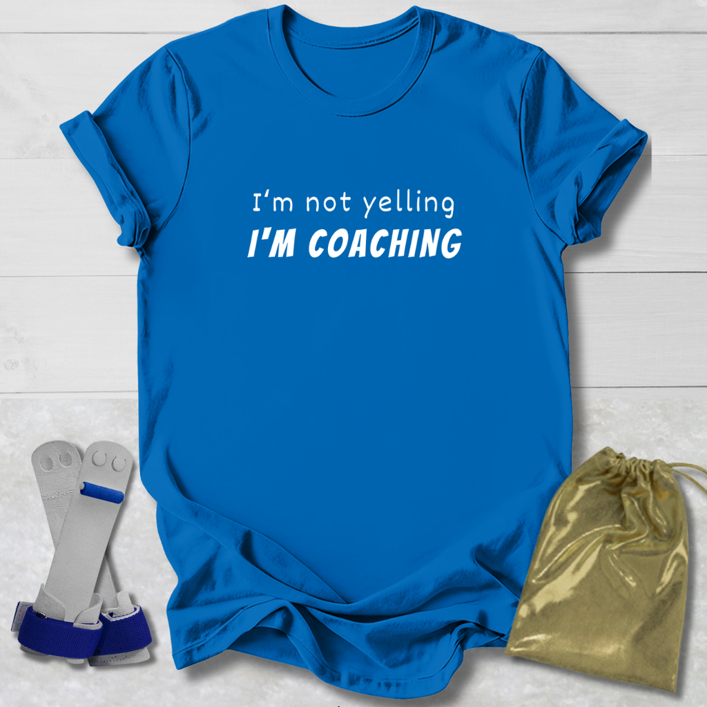 Blue t-shirt with 'I'm not yelling I'm coaching' text, socks, and drawstring bag on a light wooden surface.