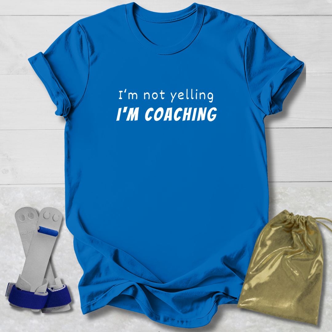 Blue t-shirt with 'I'm not yelling I'm coaching' text, socks, and drawstring bag on a light wooden surface.