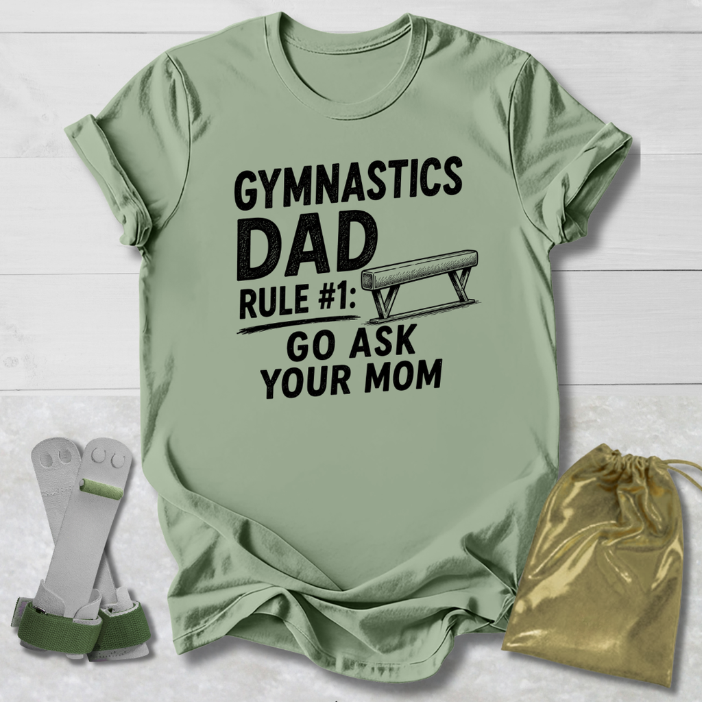 Green t-shirt with 'Gymnastics Dad' text on a wooden surface with socks and a drawstring bag.