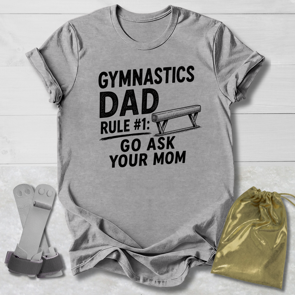 Gray t-shirt with 'Gymnastics Dad' text on a wooden surface with socks and a drawstring bag.