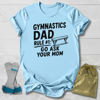 Light blue t-shirt with 'Gymnastics Dad' text, socks, and drawstring bag on a light wooden surface
