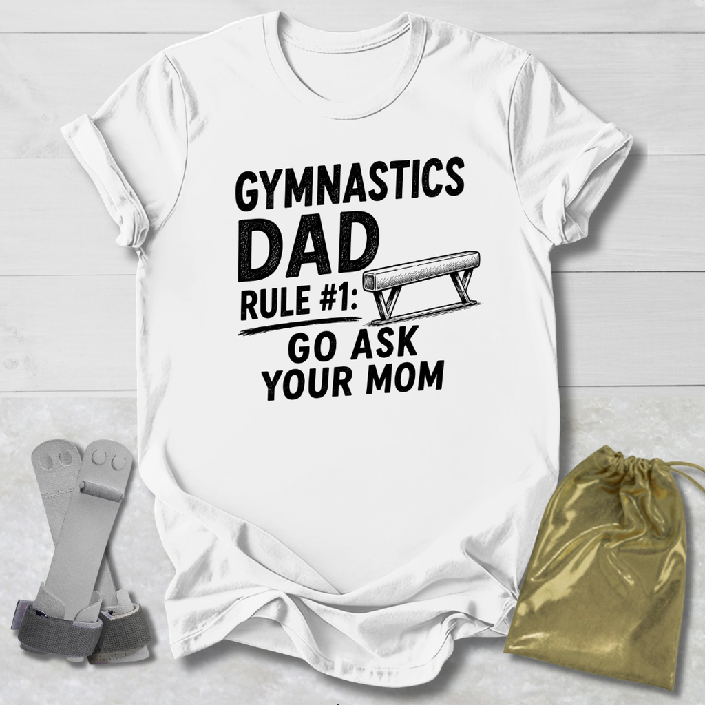 White t-shirt with 'Gymnastics Dad Rule #1: Go Ask Your Mom' text on a light wooden surface.