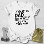 White t-shirt with 'Gymnastics Dad Rule #1: Go Ask Your Mom' text on a light wooden surface.