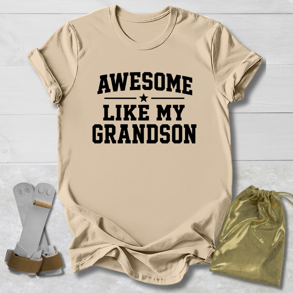 Beige t-shirt with 'Awesome Like My Grandson' text on a light wooden surface with socks and a drawstring bag.