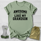 Green t-shirt with 'Awesome Like My Grandson' text, socks, and drawstring bag on a light wooden surface.