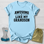 Light blue t-shirt with 'Awesome like my grandson' text, socks, and drawstring bag on a light wooden surface.