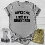 Gray t-shirt with 'Awesome Like My Grandson' text on a wooden surface with socks and a drawstring bag.