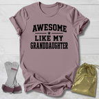 Mauve t-shirt with 'Awesome Like My Granddaughter' text, socks, and drawstring bag on a light wooden surface.