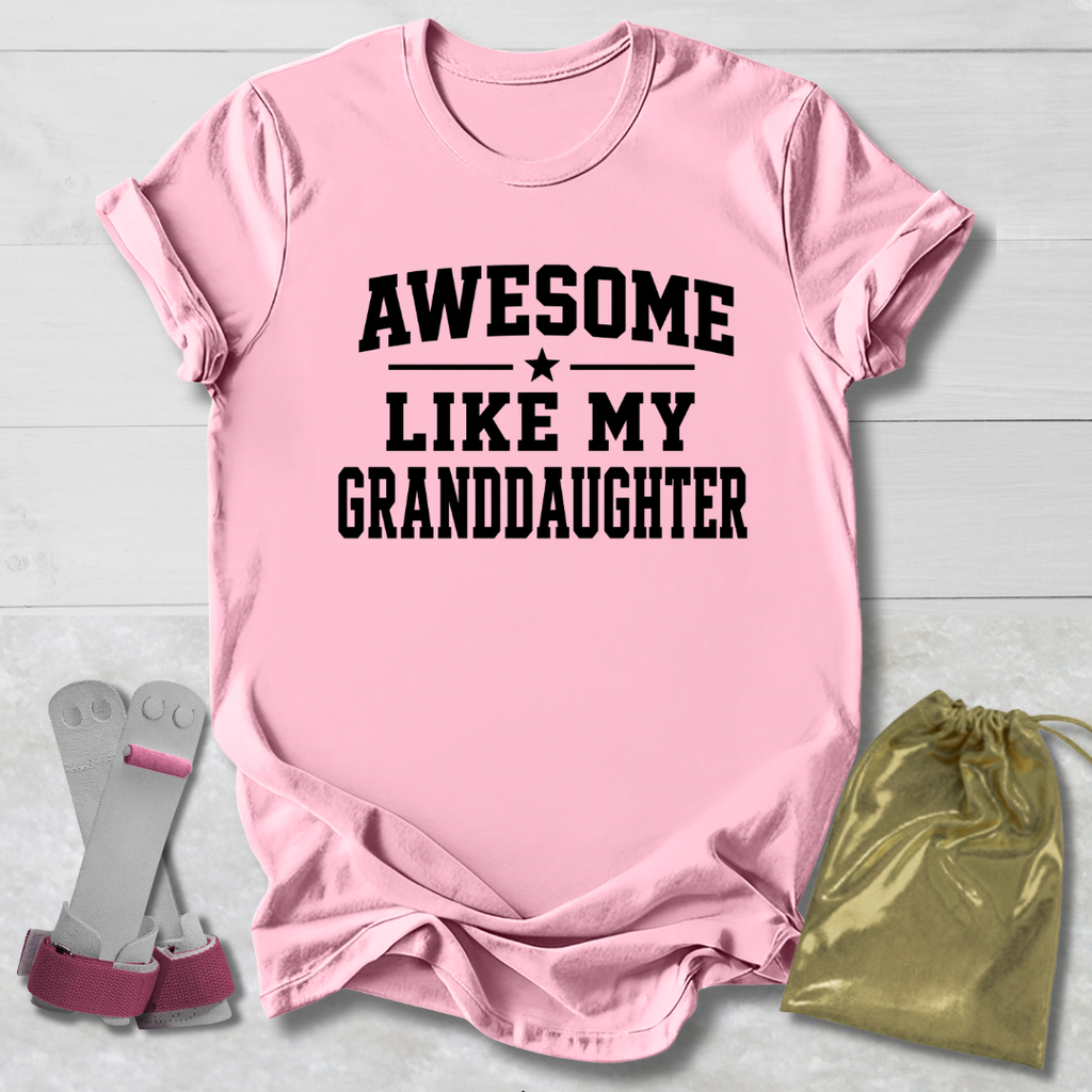Pink t-shirt with 'Awesome Like My Granddaughter' text, socks, and drawstring bag on a light wooden surface.