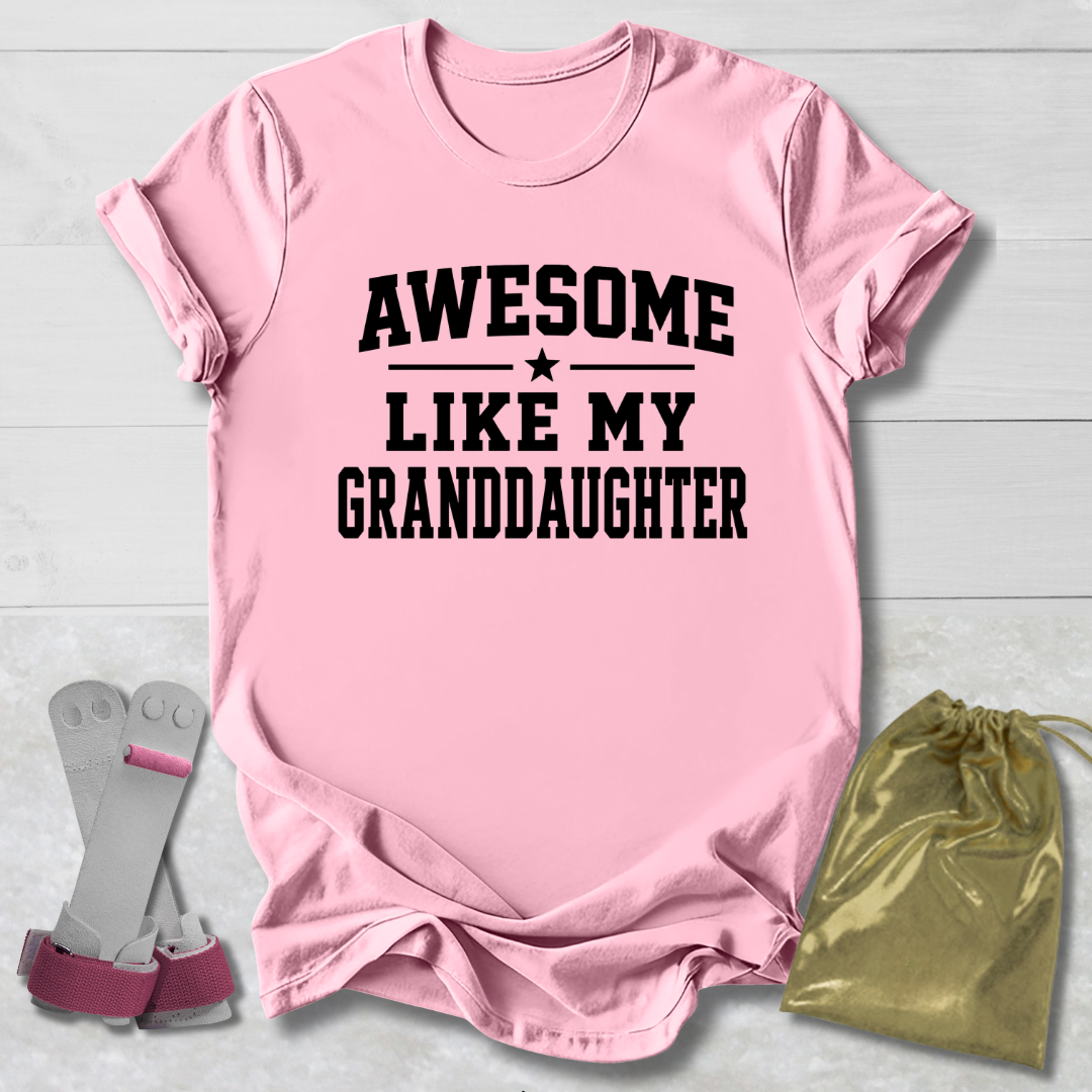 Pink t-shirt with 'Awesome Like My Granddaughter' text, socks, and drawstring bag on a light wooden surface.