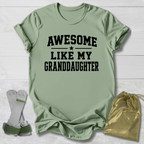 Green t-shirt with 'Awesome like my granddaughter' text, socks, and drawstring bag on a light wooden surface.
