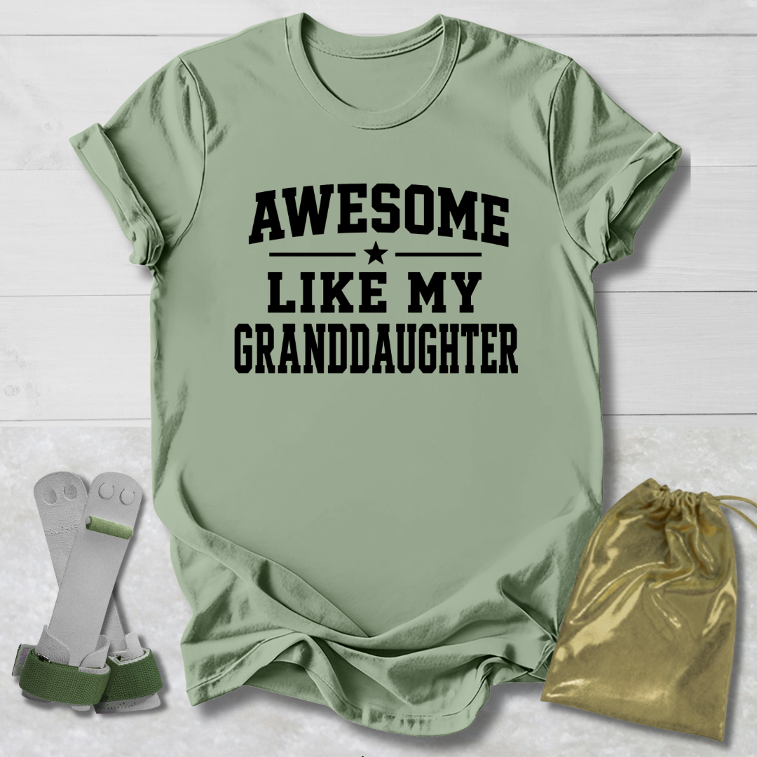 Green t-shirt with 'Awesome like my granddaughter' text, socks, and drawstring bag on a light wooden surface.