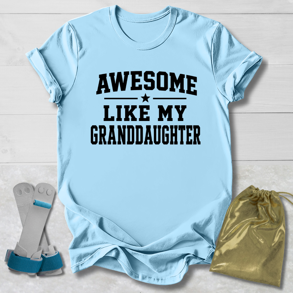 Light blue t-shirt with 'Awesome like my granddaughter' text, socks, and drawstring bag on a light wooden surface.