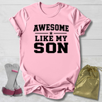 Pink t-shirt with 'Awesome Like My Son' text, socks, and drawstring bag on a light wooden surface.