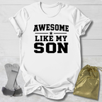 White t-shirt with 'Awesome Like My Son' text on a light wooden surface.